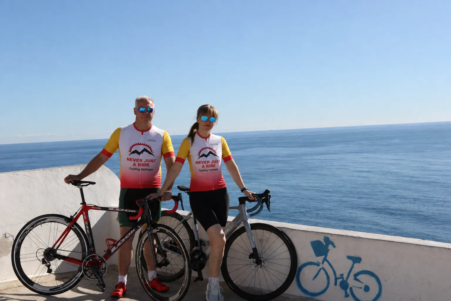 Andy and Weronika wearing Never Just a Ride cycling jerseys beside the Mediterranean